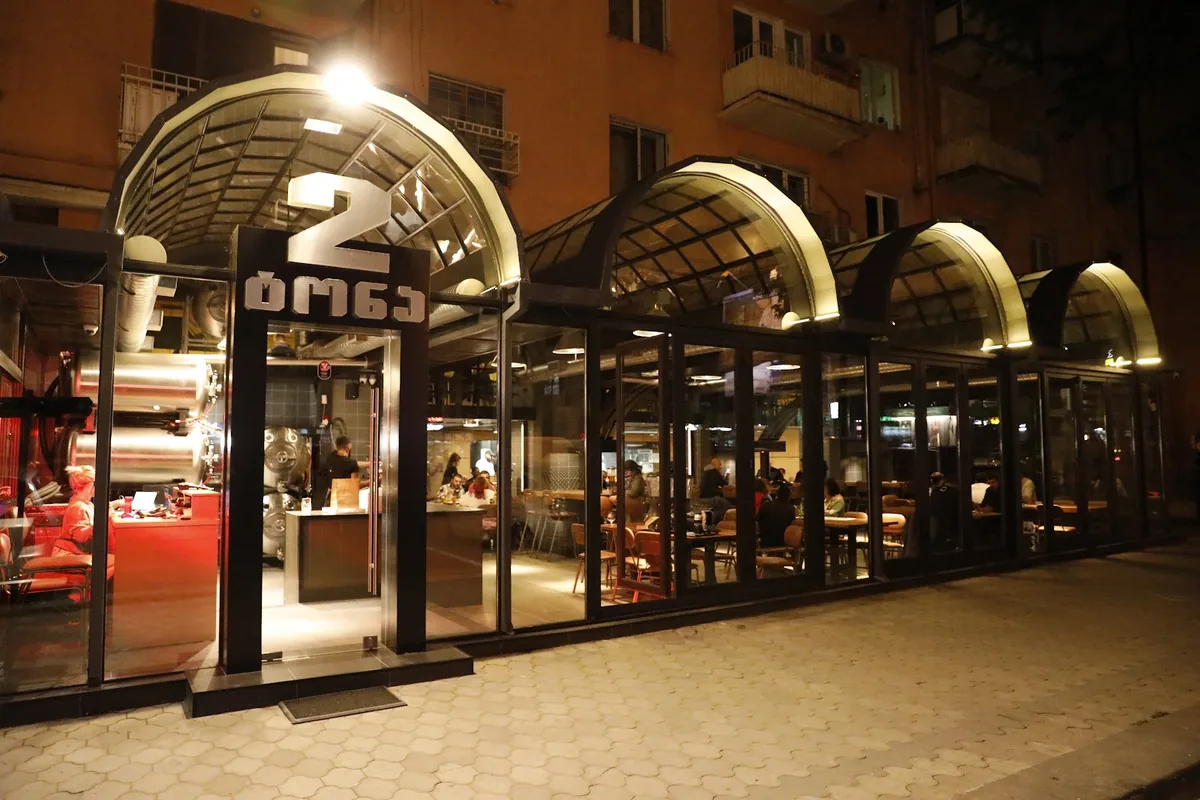The arched glass front at night, with the brewing tanks and tables inside, at 2 Tona on Vazha-Pshavela Avenue