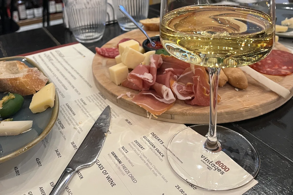 A glass of white wine next to a cheese and charcuterie board on an 8000 Vintages menu