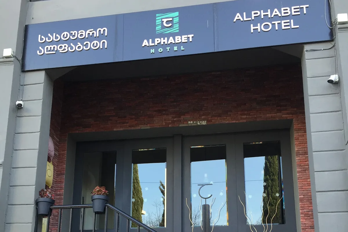 The entrance of Alphabet Hotel on Telavi Street in Avlabari, its sign above glass double doors in a red brick porch