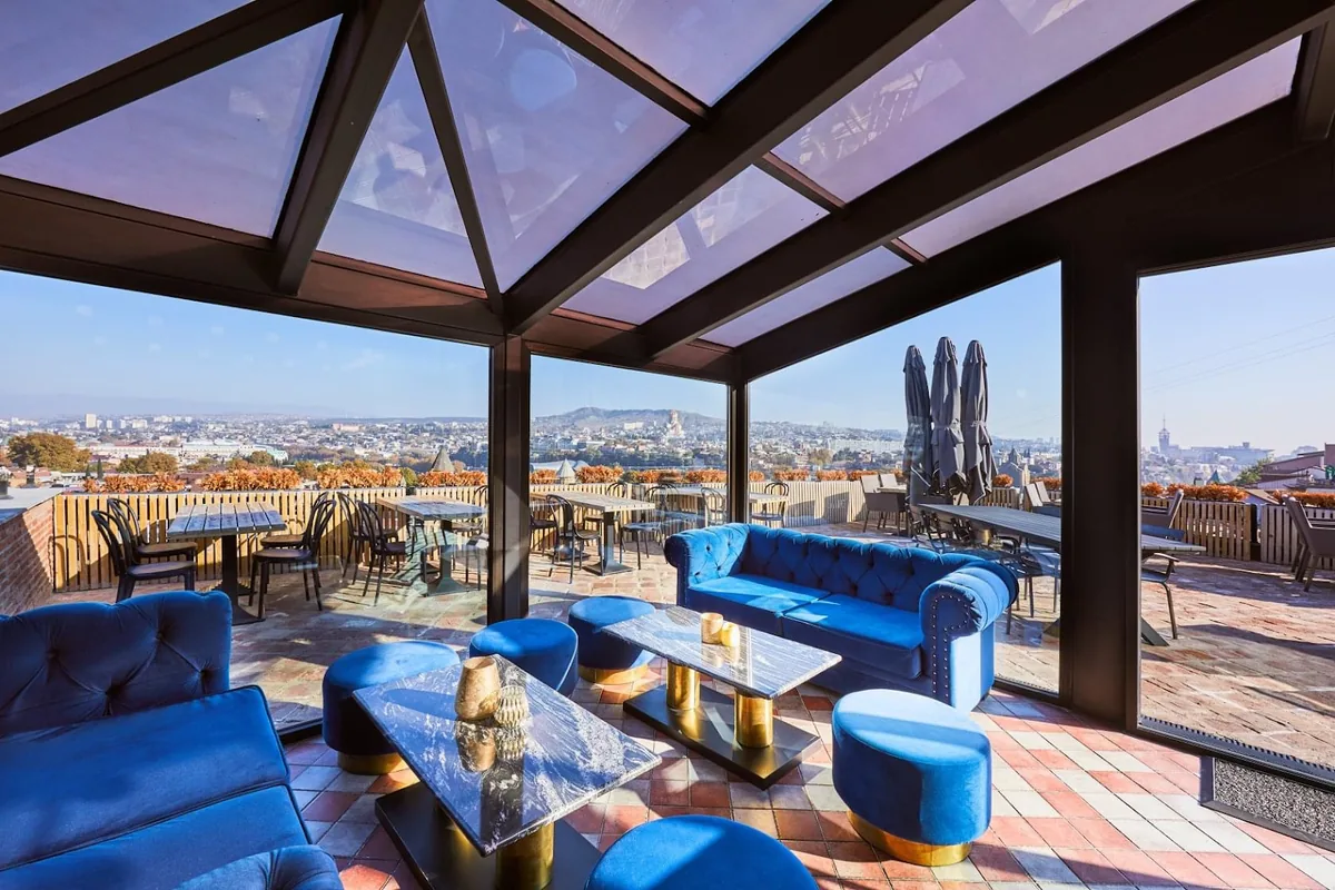 Glass-roofed rooftop terrace with blue velvet sofas and views over Tbilisi at Amante Narikala Boutique Hotel