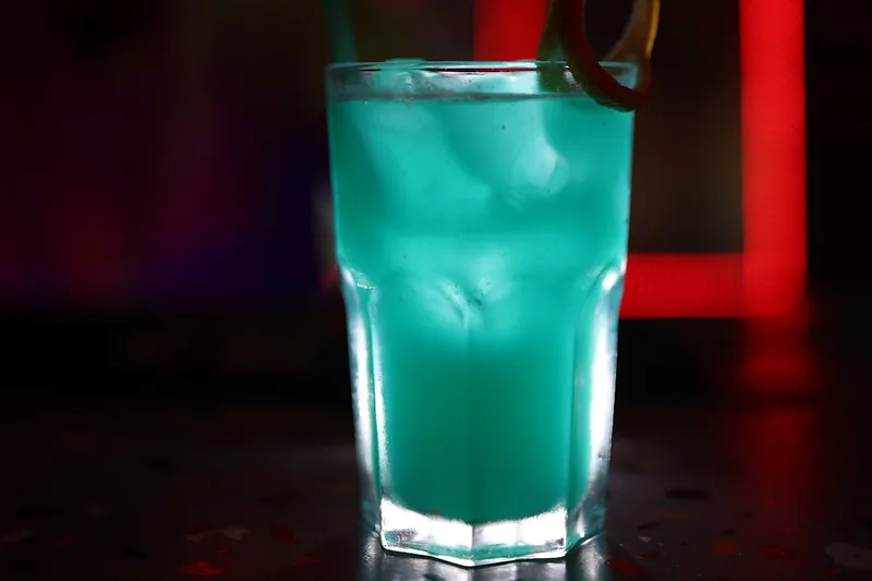Cyan blue cocktail with peel garnish and straw in a tall glass at AMBAVI