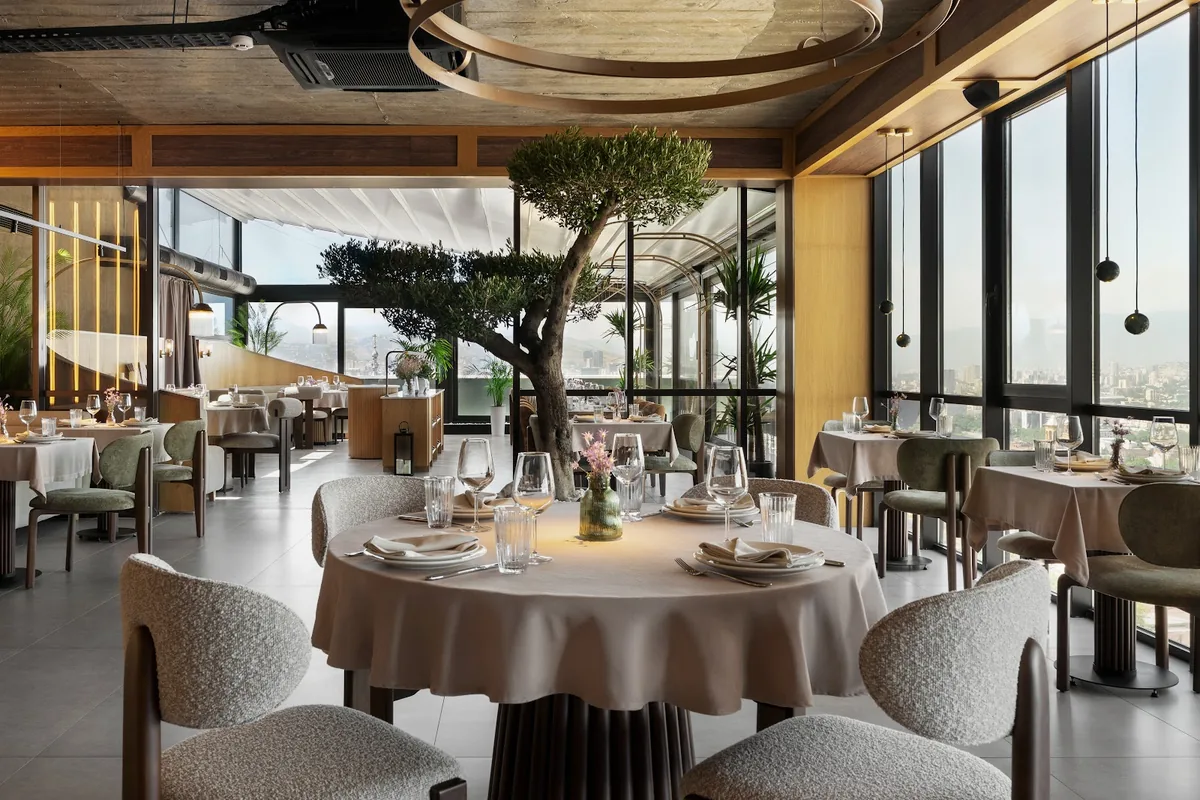 Dining room with an olive tree and floor-to-ceiling windows over the city at AMO
