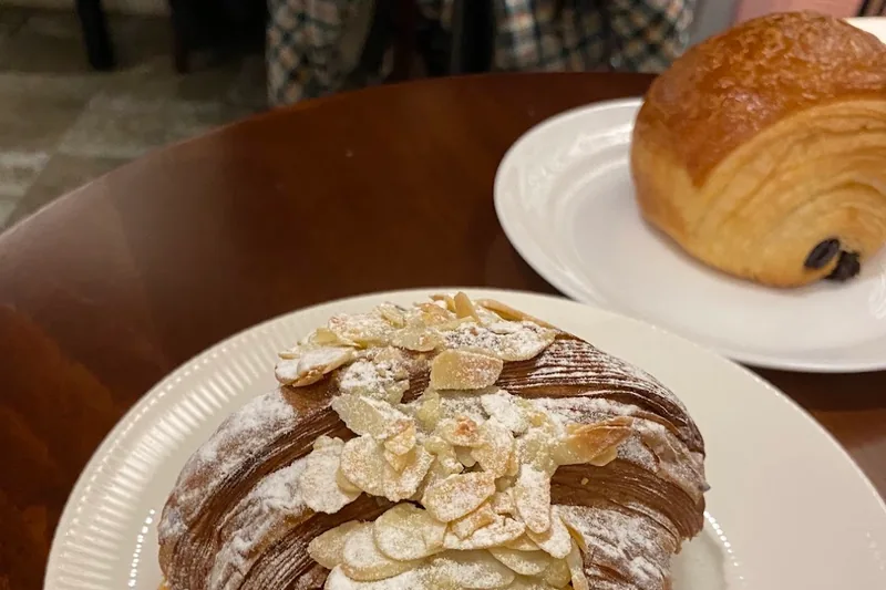 An almond croissant and a pain au chocolat on white plates at Baba Bakery