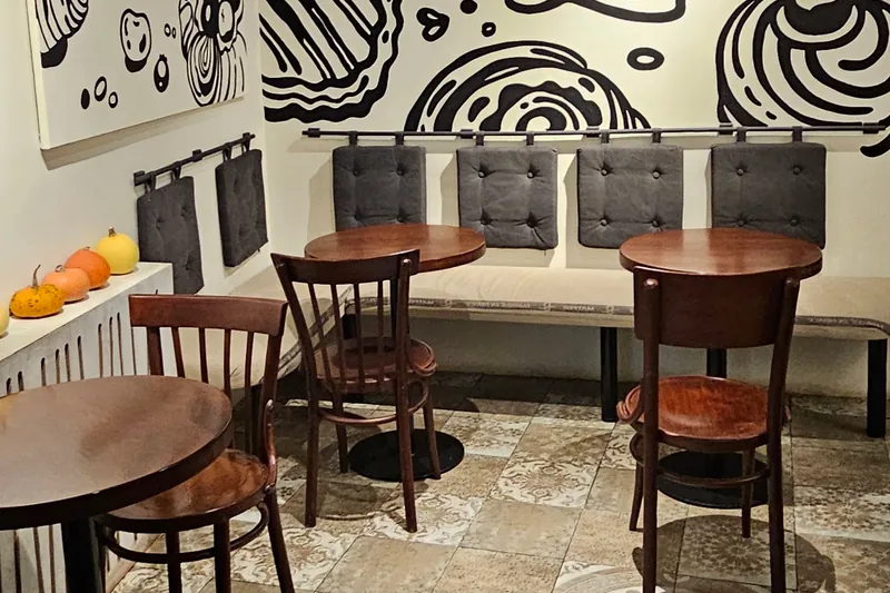 Wooden cafe tables and a cartoon pastry mural on the wall at Baba Bakery on Ivane Machabeli Street