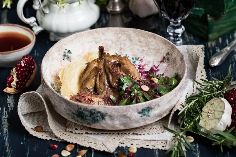 Roast quail with mashed potatoes and herbs in a patterned bowl at Barbarestan