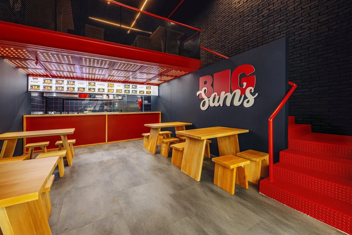 Dining area with wooden tables and red stairs at Big Sam’s Galleria Tbilisi