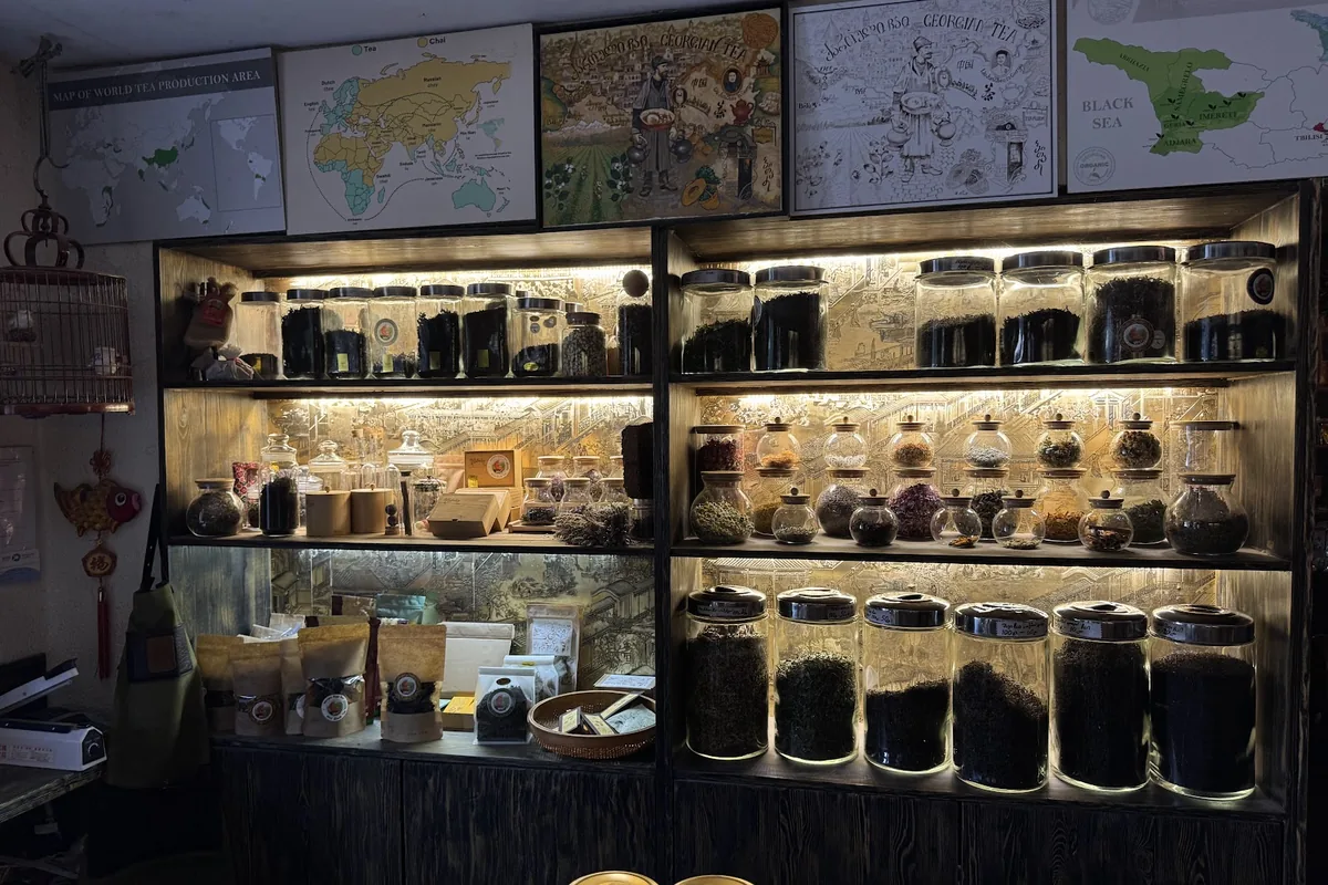 Lit shelves of loose-leaf tea jars under framed maps of Georgian tea regions at the Bitadze tea shop on Galaktion Tabidze Street
