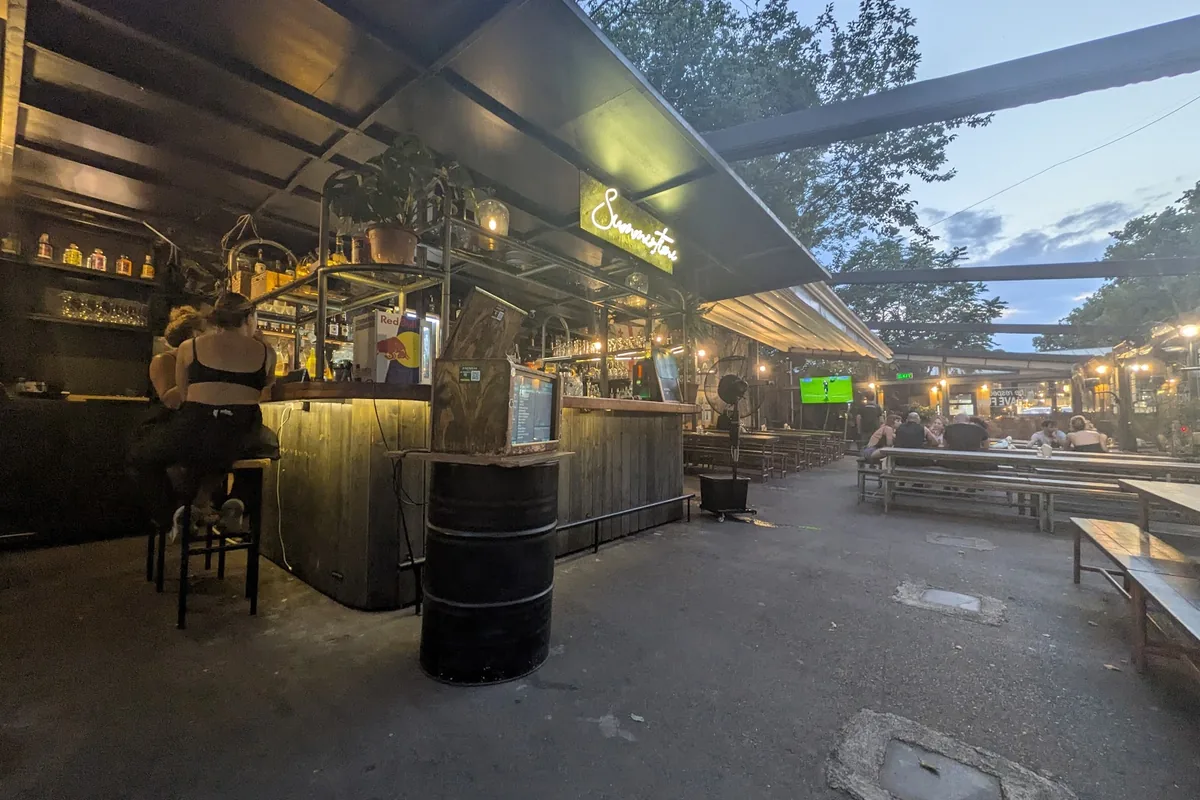 Open-air bar counter and long communal tables in the shared courtyard of Wine Factory N1 at dusk