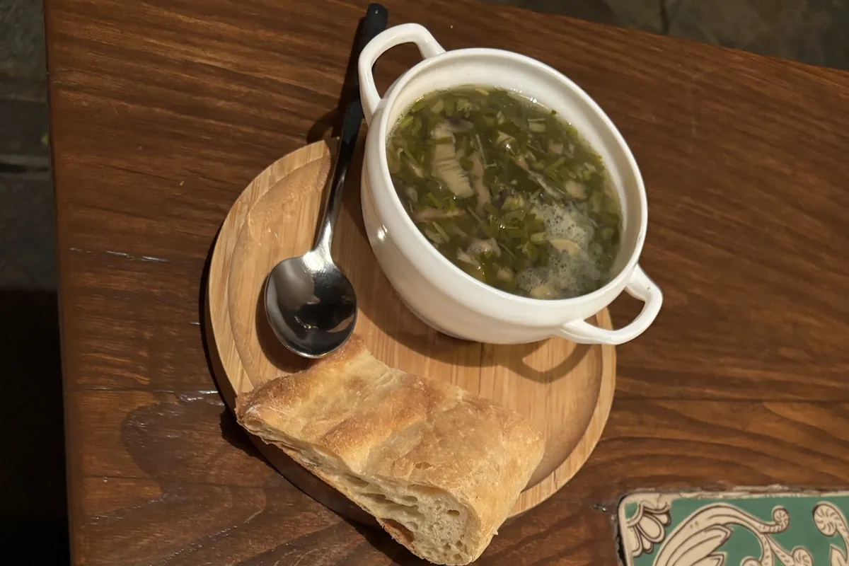 Mushroom soup with chopped herbs and a slice of bread at Café Leila