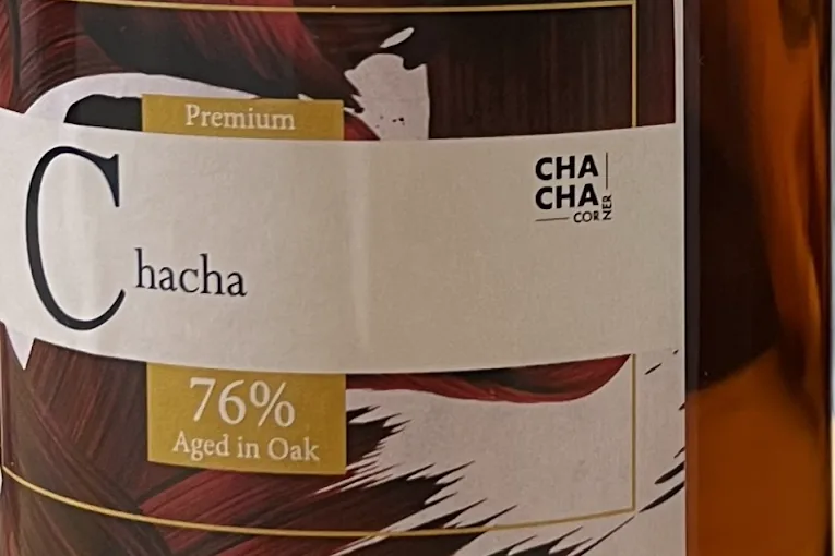 Label of a Chacha Corner bottle of premium chacha aged in oak, with the amber spirit showing through the glass