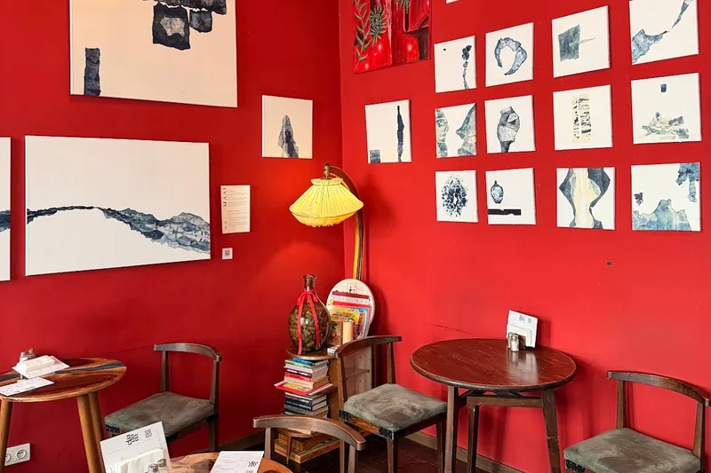 Red room with art-covered walls and wooden tables at Chaduna