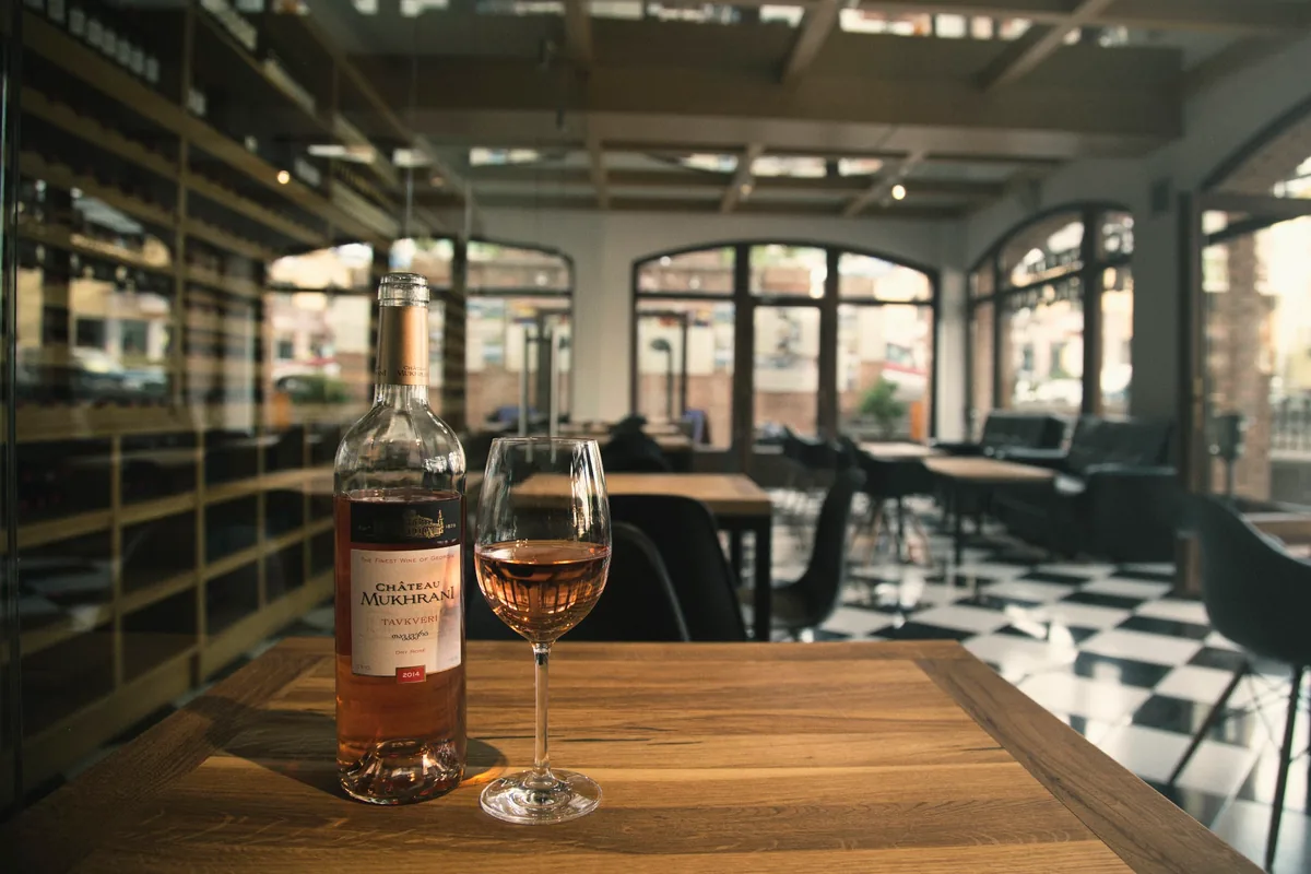 A bottle of rosé and a glass of wine on a wooden table at the Chateau Mukhrani wine bar