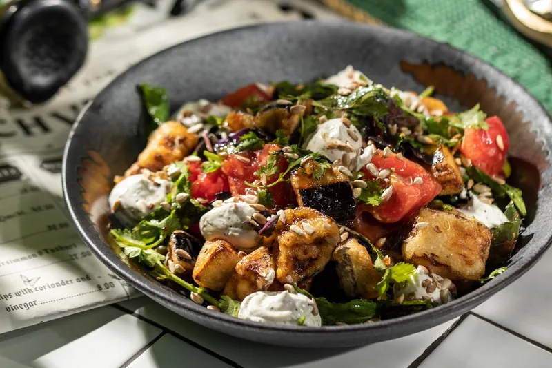 Fried eggplant salad with tomatoes and creamy dressing in a dark bowl at Chveni