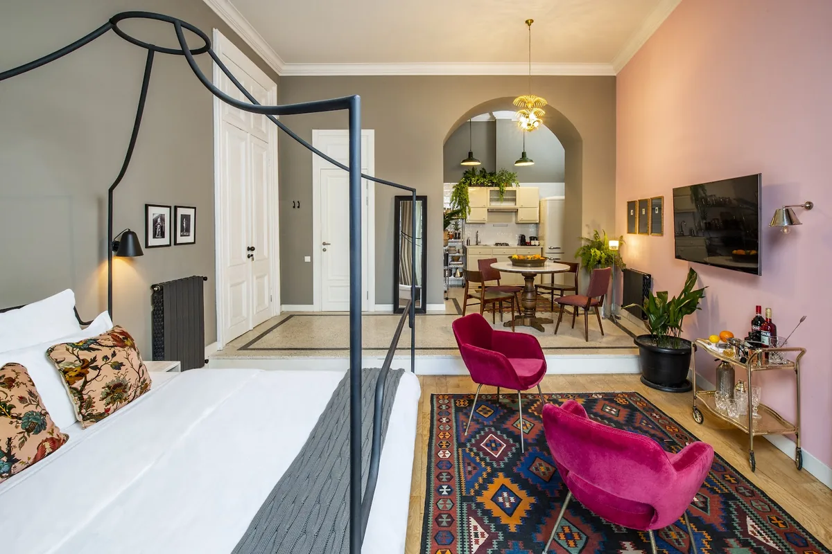 Guest room with a four-poster bed and pink armchairs at Communal Sololaki