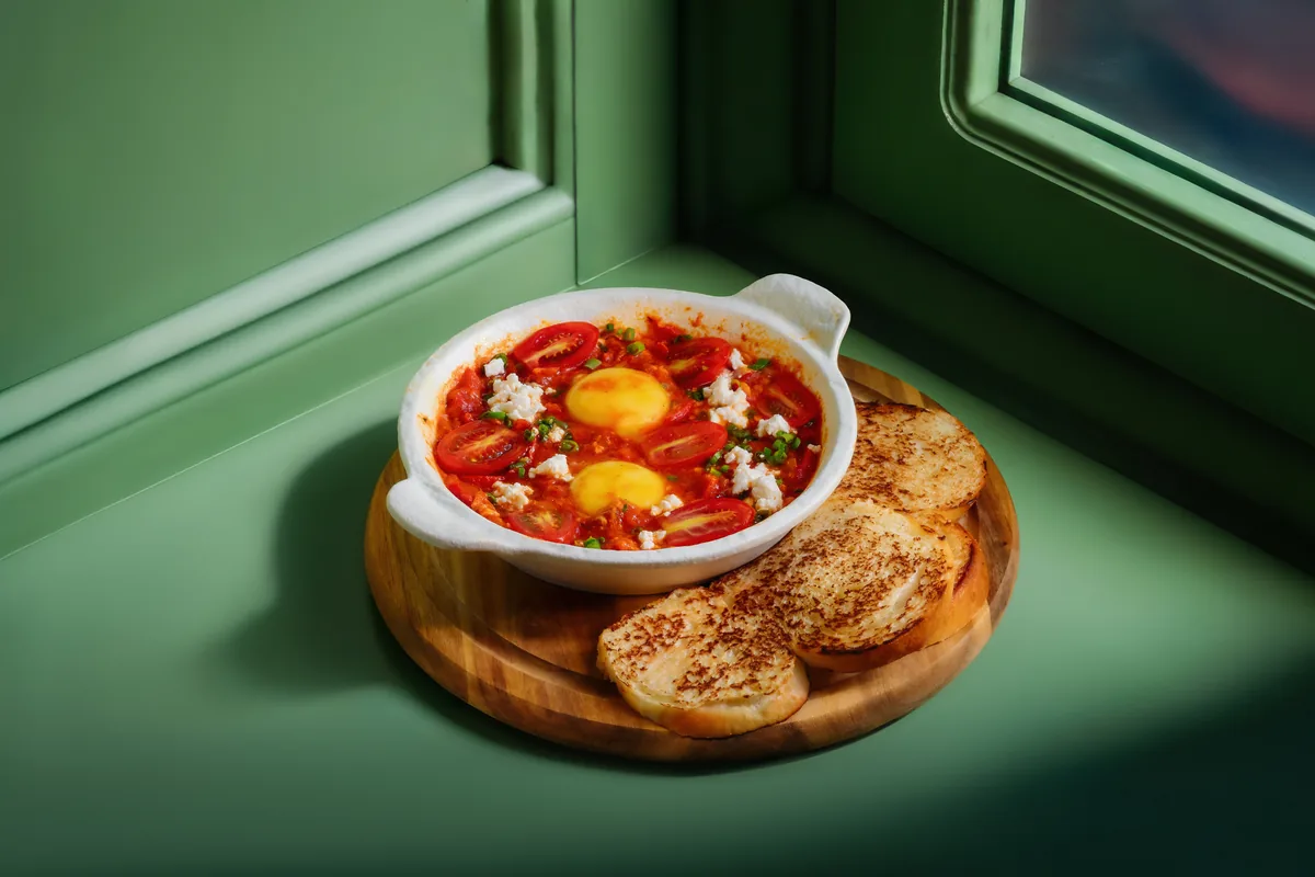 Shakshuka in a white dish with toasted bread on a wooden board at Crossroads Bistro