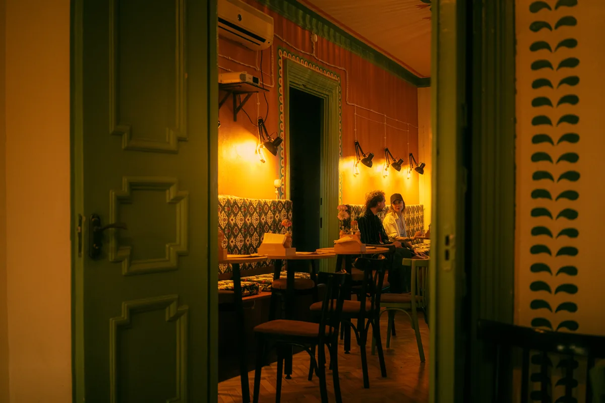 Dining room with a patterned banquette and wall lamps seen through a green door at Crossroads Bistro