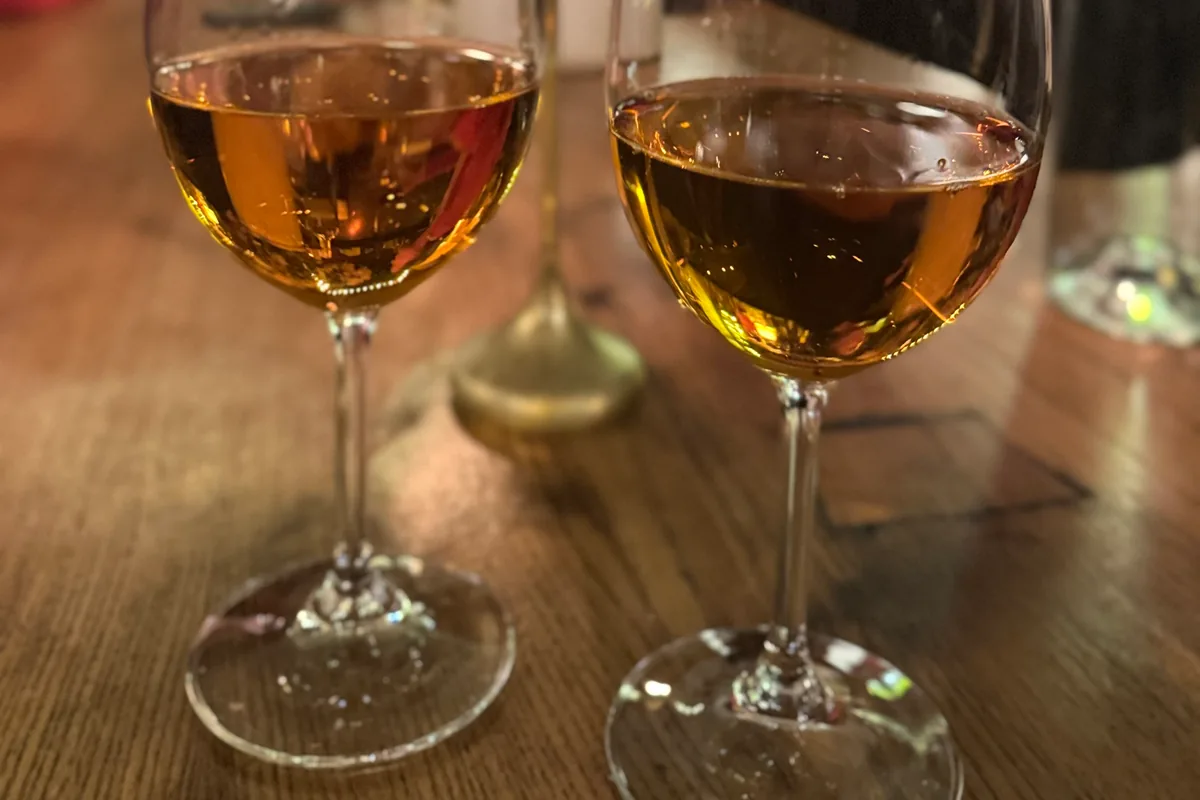 Two glasses of amber wine on a wooden table at DADI Wine Bar & Shop
