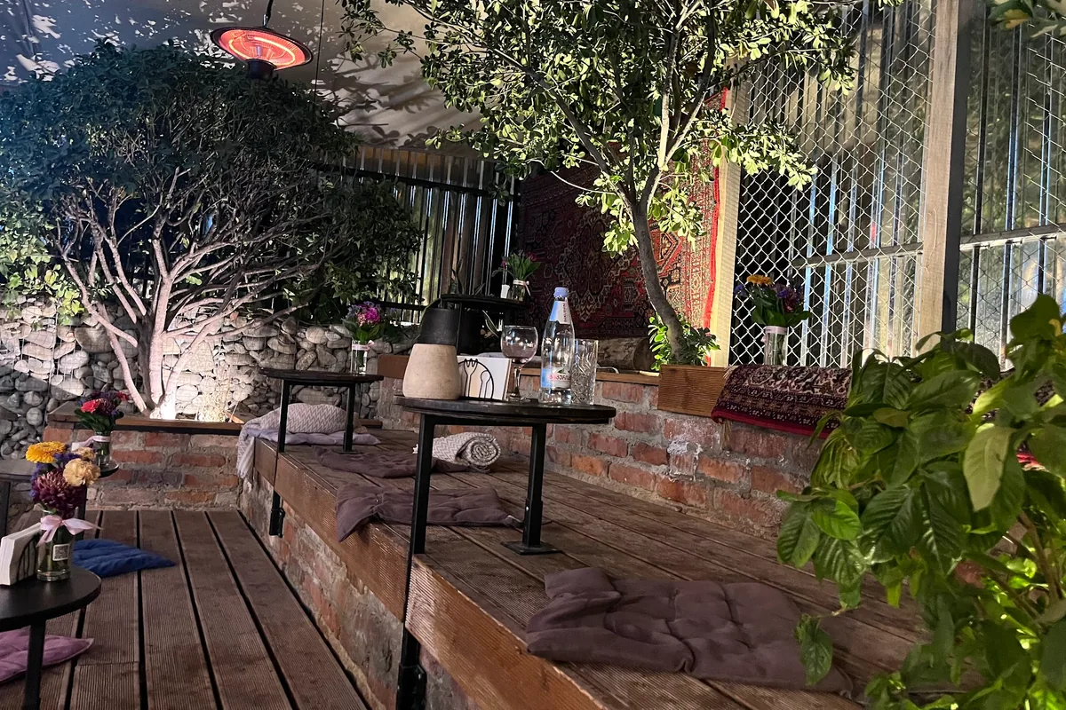 Outdoor tiered wooden terrace with trees and low tables at DEDA Tbilisi