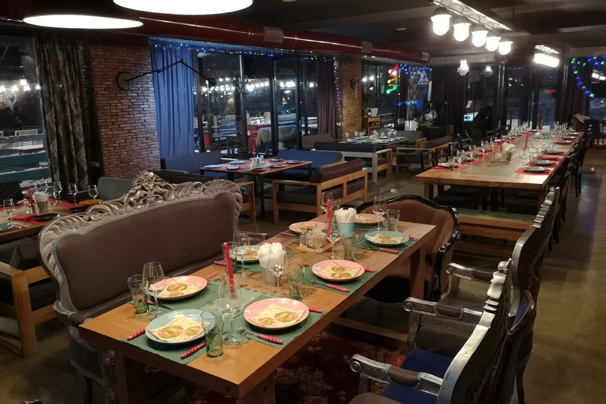 Long set tables, carved silver armchairs and big windows in the dining room at Drunk Cherry in Gudauri