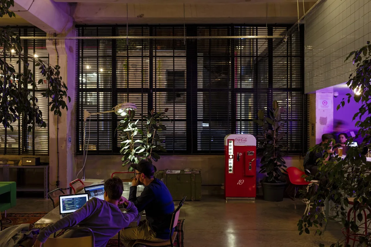 The ground-floor lounge at Fabrika, with rugs, rubber plants, a vintage Coca-Cola fridge and guests working on laptops by the factory windows
