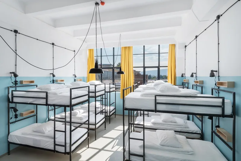 Bunk-bed dorm room with tall factory windows and yellow curtains at Fabrika Hostel & Suites