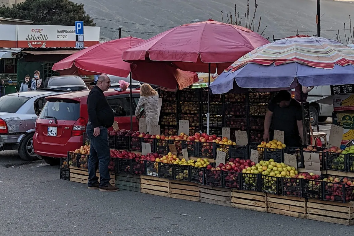 Fruit stalls under red and striped umbrellas at the Navtlughi farmers market in Samgori