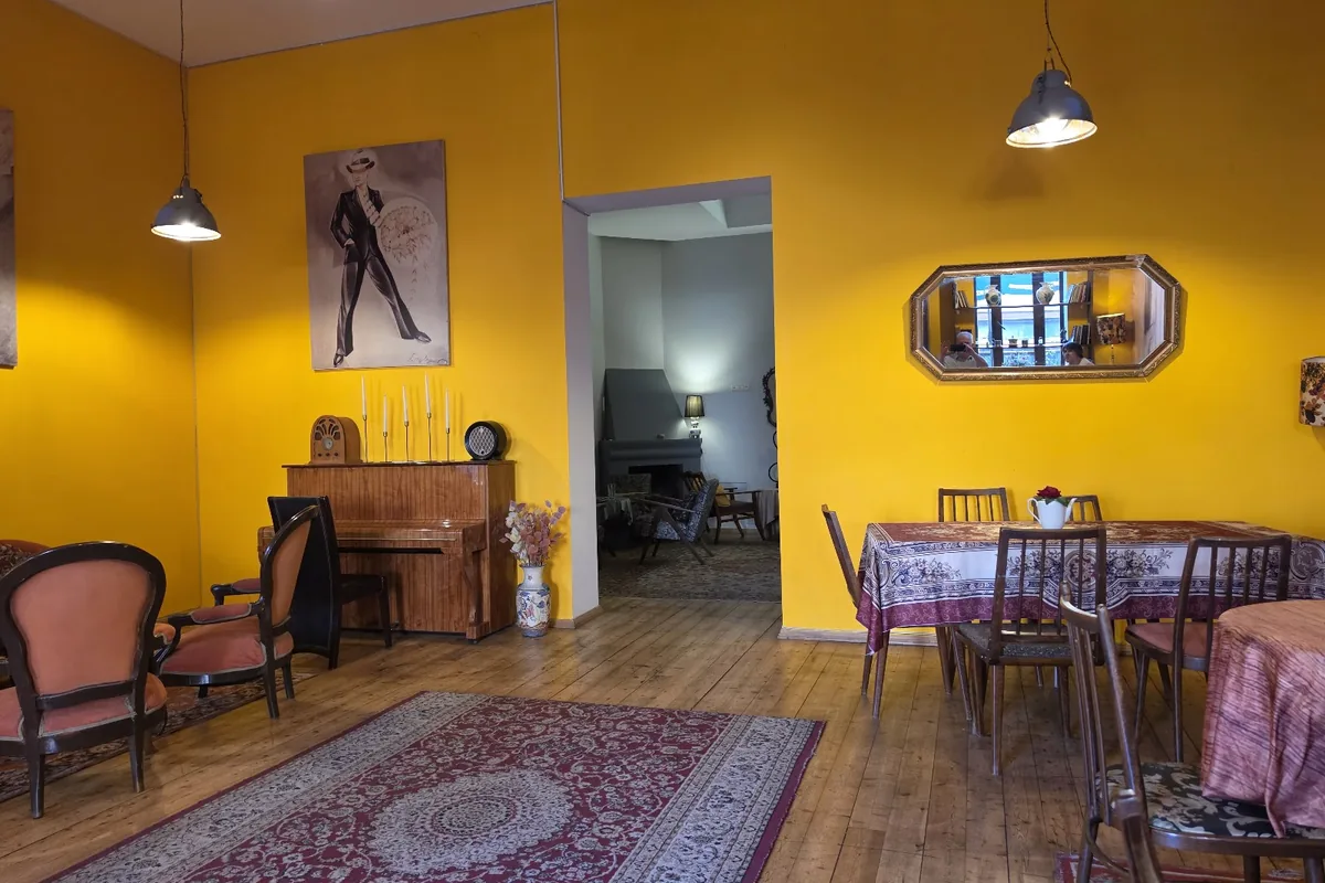 The yellow-walled room at Foe-Foe Tea House in Kutaisi, with an old piano, velvet armchairs and a rug on the wooden floor