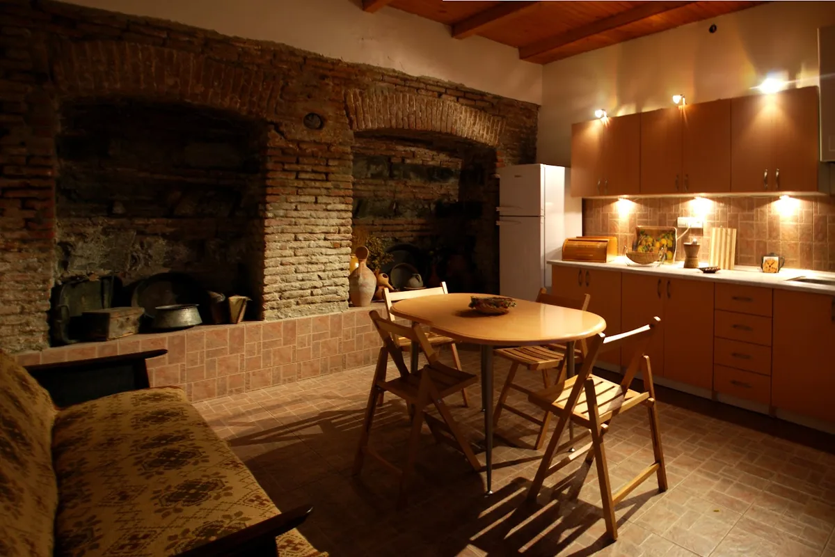 Shared kitchen at Green House Hostel, with an old brick hearth wall, a wooden dining table and folding chairs