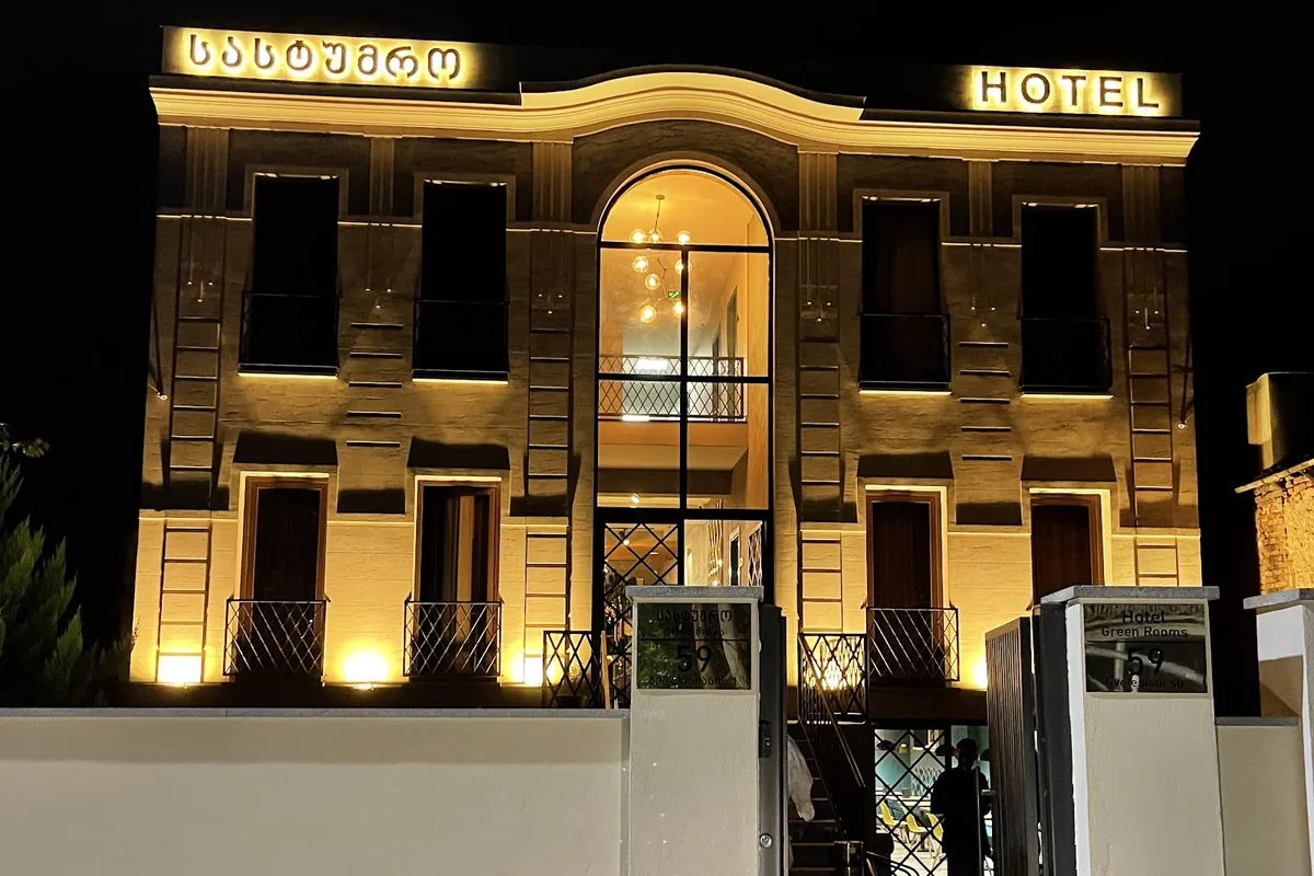 The front of the Green Rooms hotel in Kutaisi lit up at night, with its arched glass entrance behind a gated wall