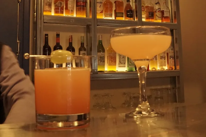 Two cocktails, one in a rocks glass and one in a coupe, on the bar at G.U.M in Fabrika