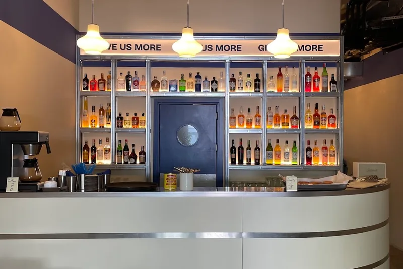 Curved white bar counter and lit back bar shelves at G.U.M cocktail bar in Fabrika