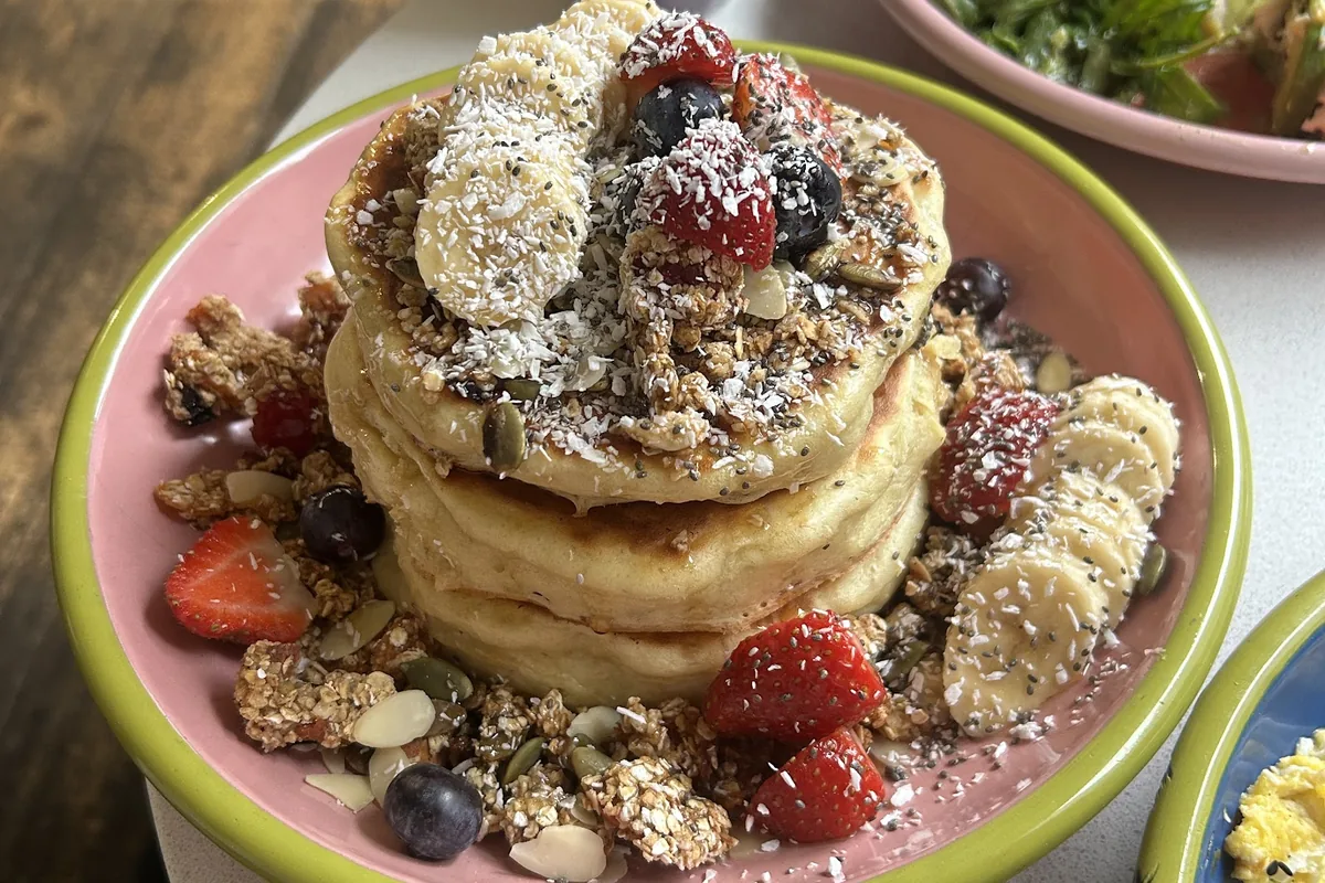 Stack of pancakes with strawberries, banana, blueberries and granola at Hello Breakfast