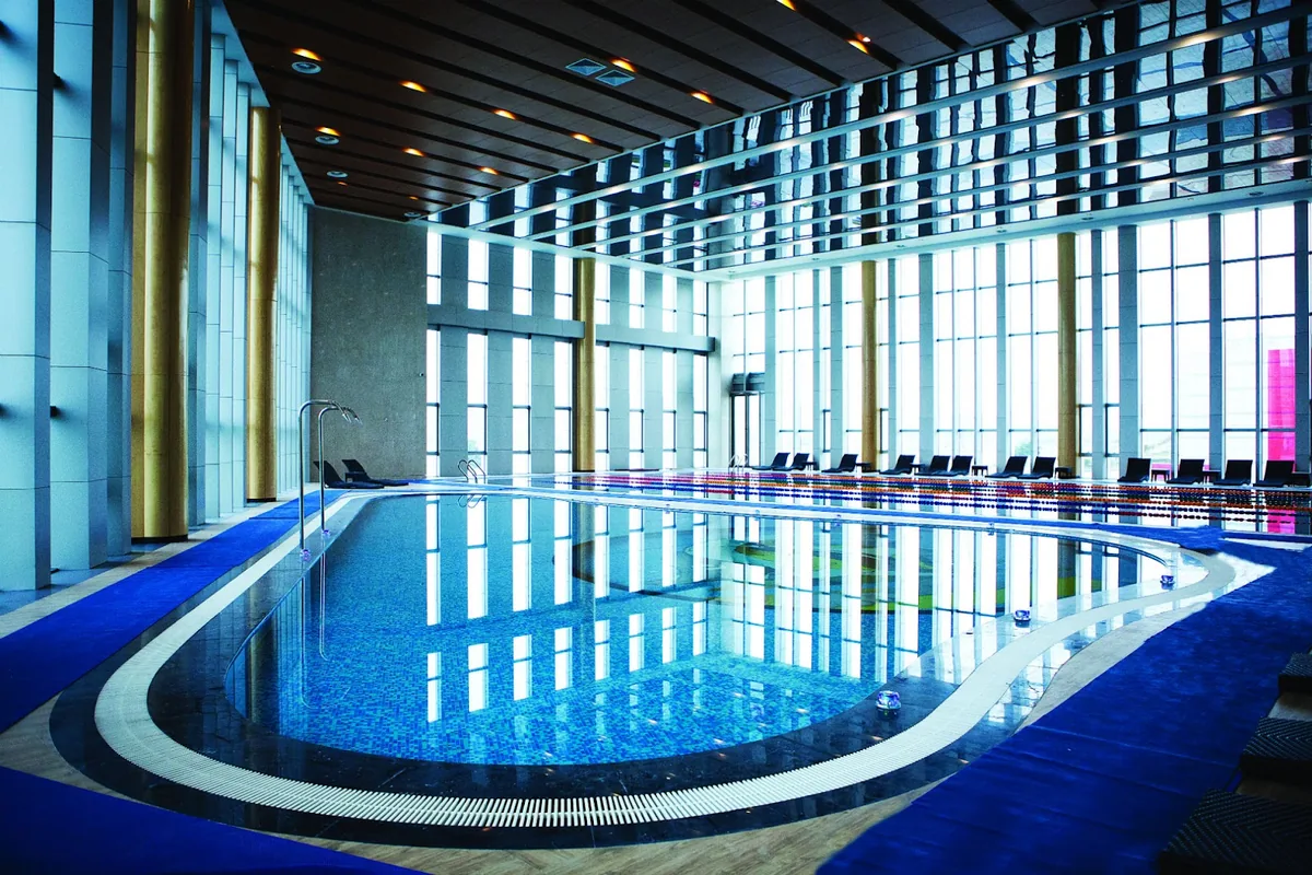 The indoor pool at Hualing Tbilisi under floor-to-ceiling windows, with loungers along the far side