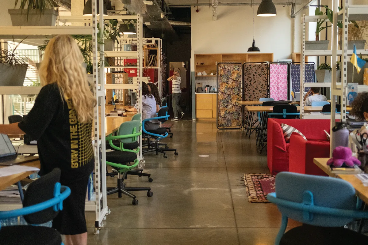 Shared desks, white shelving with plants and red sofas in the coworking space at Fabrika