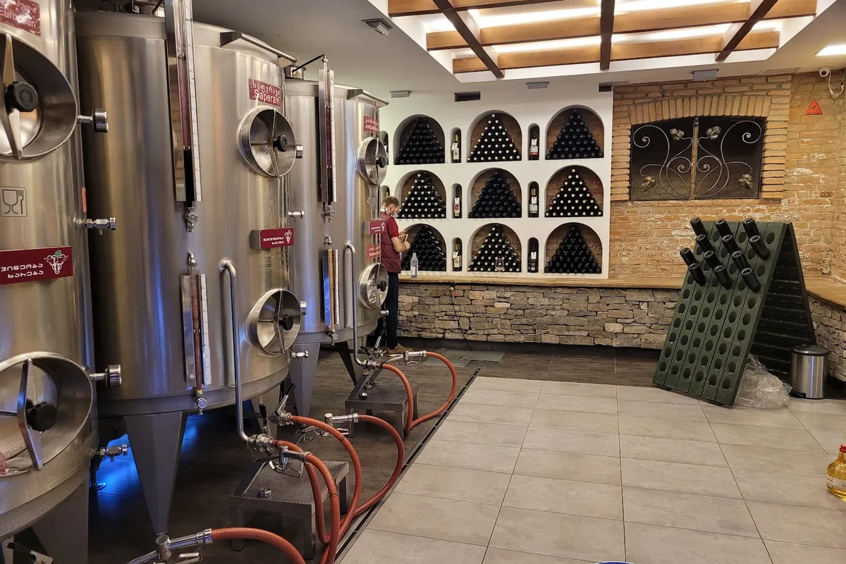 Steel wine tanks beside arched bottle niches and a brick wall at Khareba's wine shop on Rustaveli Avenue
