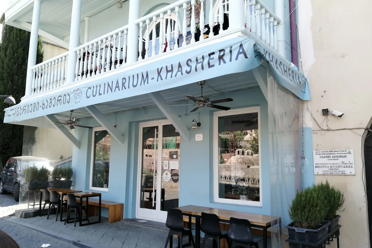 Pale blue front of Culinarium-Khasheria with its Khasheria awning and street tables, the Abanotubani bath domes reflected in the window, Tbilisi