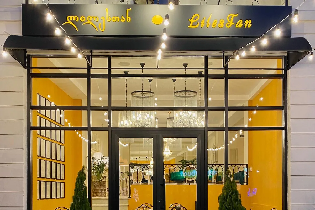 The glass front of Lilestan in Kutaisi at dusk, with its sign above and yellow walls and chandeliers inside