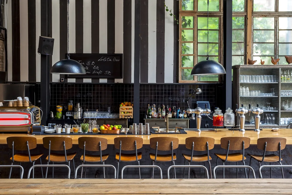 Long wooden bar counter with a row of stools, black and white striped walls and tall factory windows at Lolita
