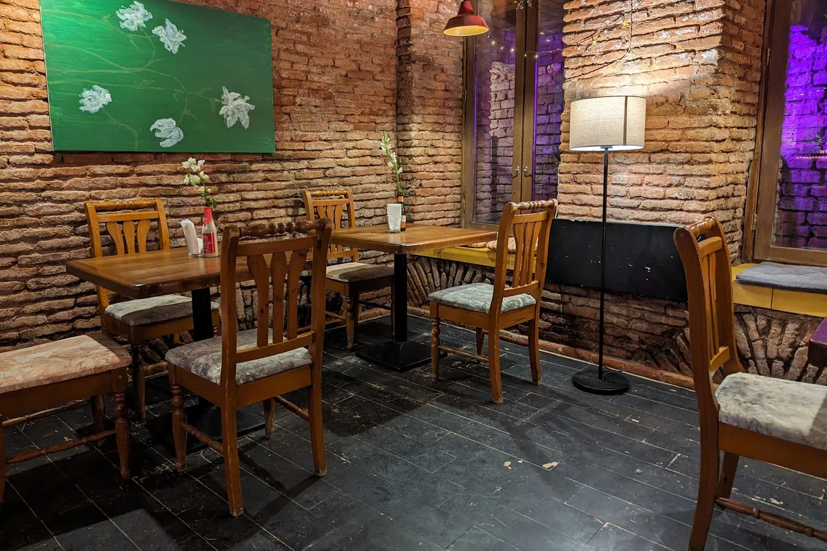 Brick-walled room with wooden tables and a green painting at Lutra Lutra Bar