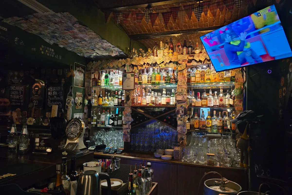 Back bar bottle shelves with banknotes and tv at MacLaren's Irish Pub