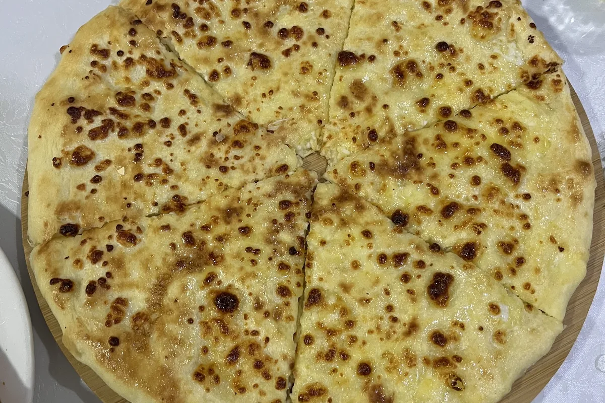 Megrelian khachapuri with cheese baked on top, cut into slices on a wooden board at Mapshalia