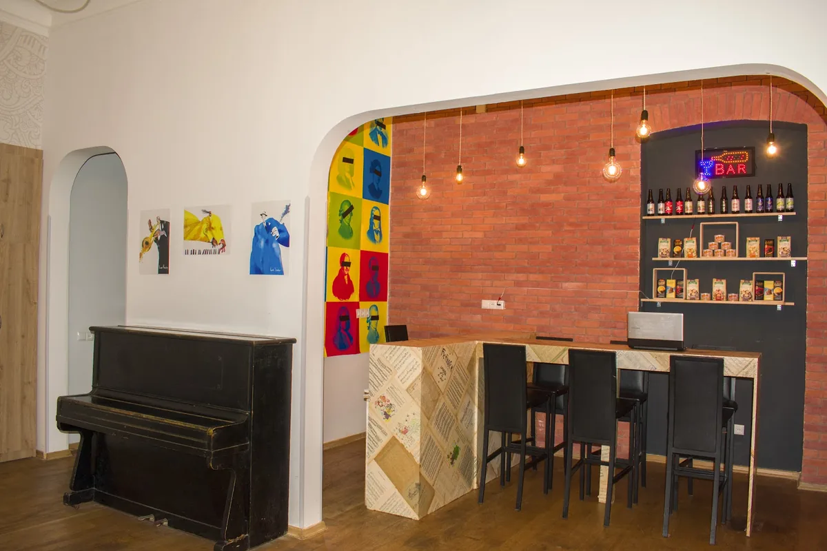 Common room at Moosica Hostel, with an upright piano, composer pop-art posters and a small brick-walled bar