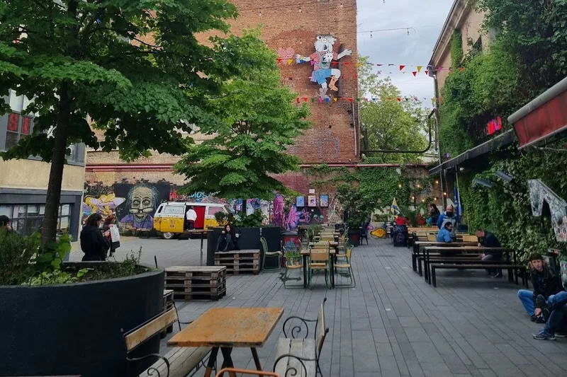 Open-air tables under pennant bunting in the Fabrika courtyard outside Moulin Électrique, with a mural on the wall behind
