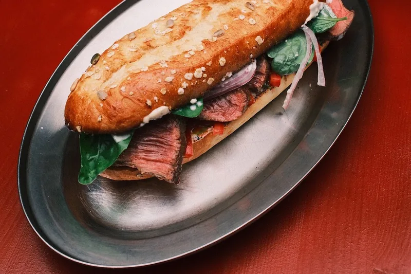 Steak sandwich on an oval metal plate with crinkle-cut fries at Mova Maisi