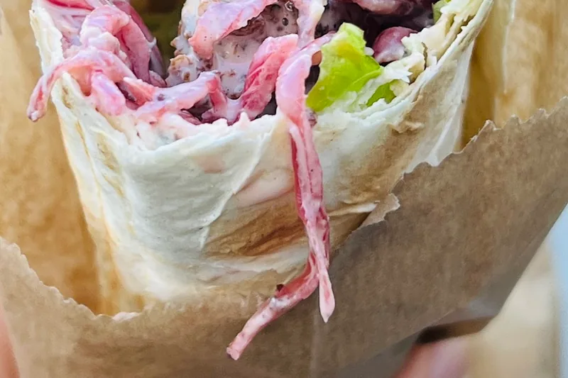 Falafel wrap with purple cabbage in a paper sleeve at Muhudo