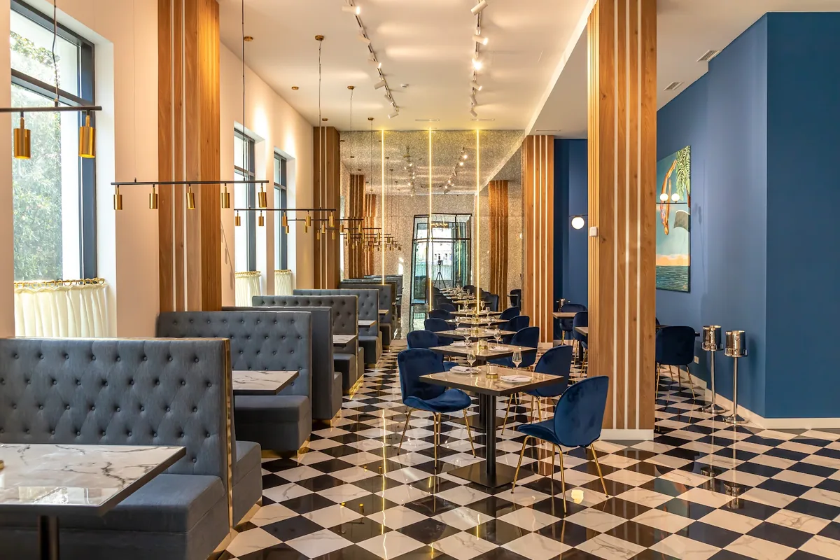 The dining room at Newport Hotel Kutaisi, with blue walls, blue velvet chairs, tufted booths and a checkered marble floor