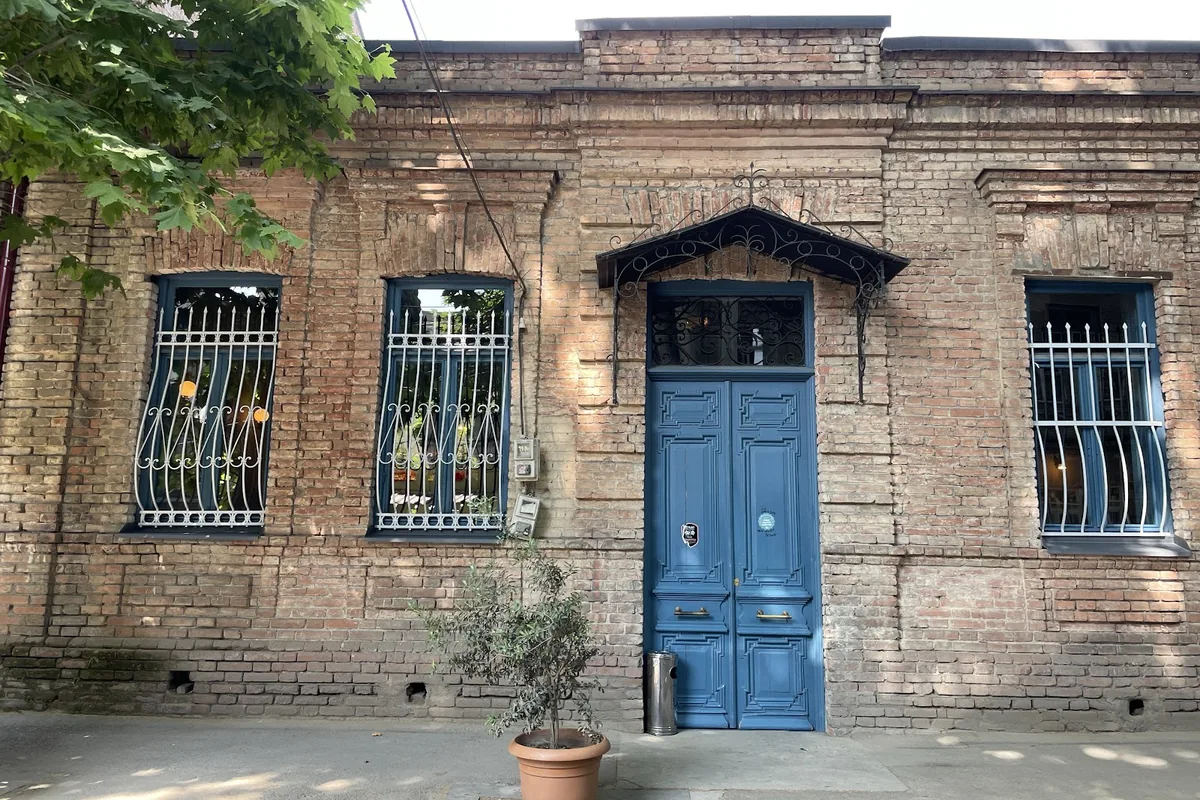 Old brick facade with a blue double door and barred windows at Ninia's Garden
