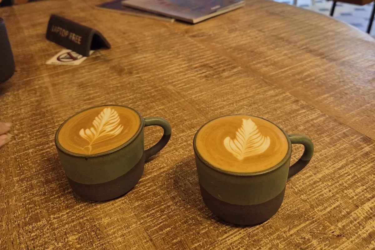 Two cappuccinos with latte art on a wooden table at OKRO Coffee Roastery