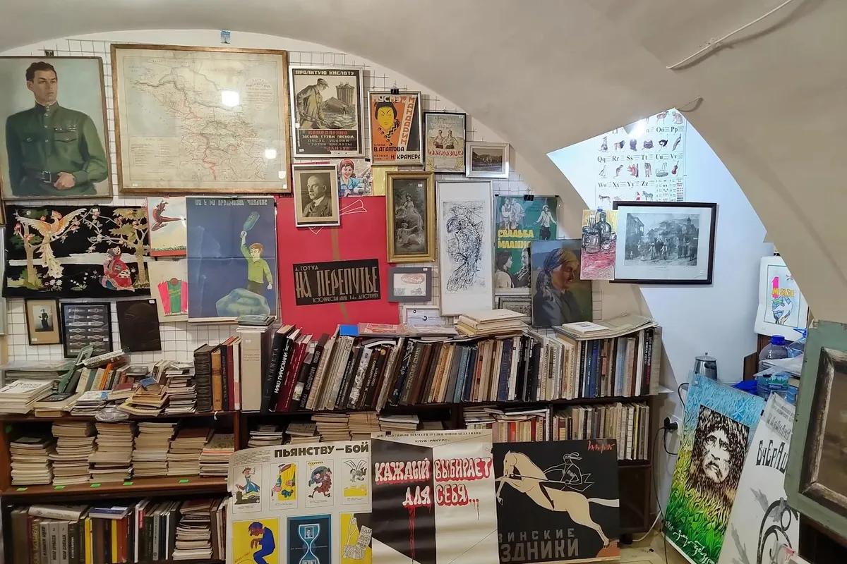 Soviet film posters, old maps and paintings above shelves of stacked Georgian and Russian books under the vaulted ceiling of Old Book Story