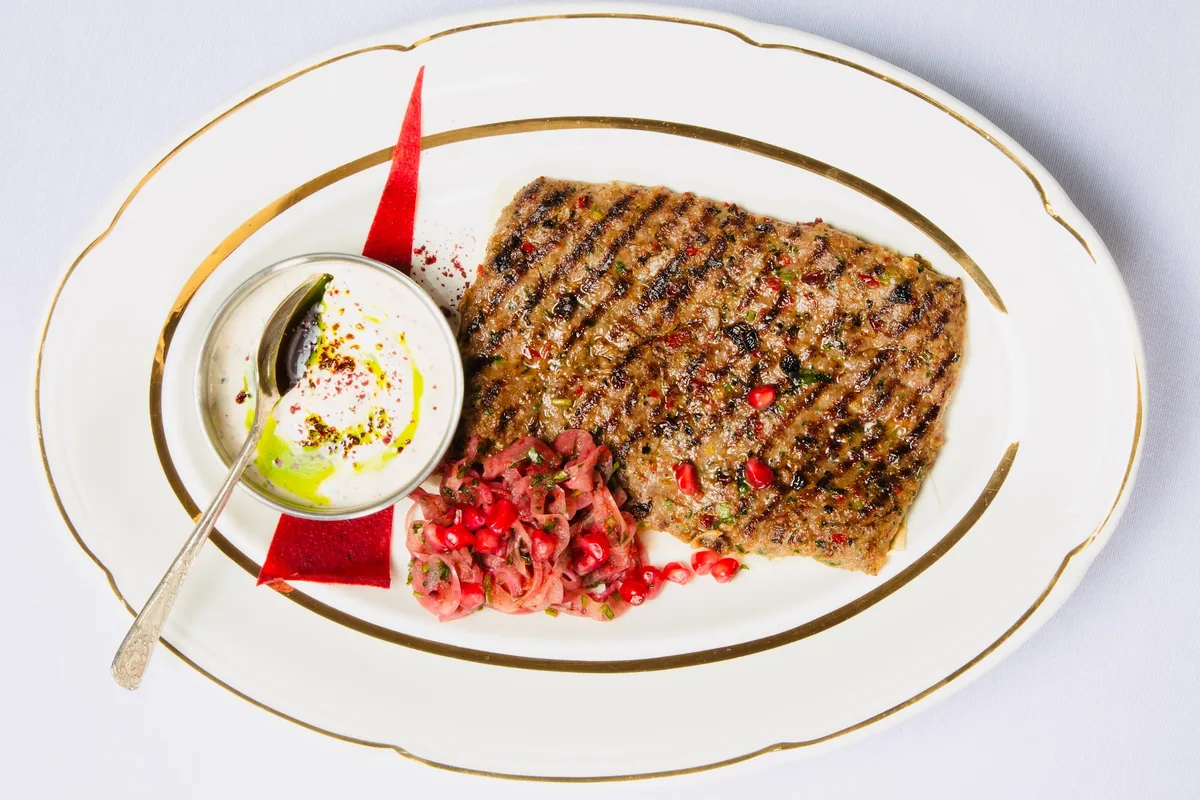 Grilled kebab with dipping sauce and pomegranate salad on an oval platter at OtsY